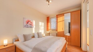 A neatly arranged bedroom with a bed, bedside tables, a wardrobe, and a painting on the wall. - House Dünenwald 14 - short distances to the beach and the center for 3 persons (Zinnowitz)