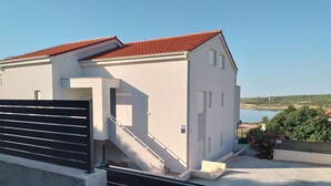 Un edificio moderno con techo de tejas rojas, una escalera que conduce a un balcón y vistas de agua y vegetación al fondo.