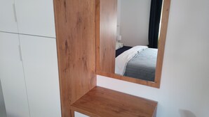 Un dormitorio con un armario de madera, una mesita de noche y un espejo que refleja una cama con colcha azul y blanca a rayas.