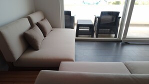 Un salón moderno con un sofá y una butaca, suelo de madera y vistas a través de un ventanal.