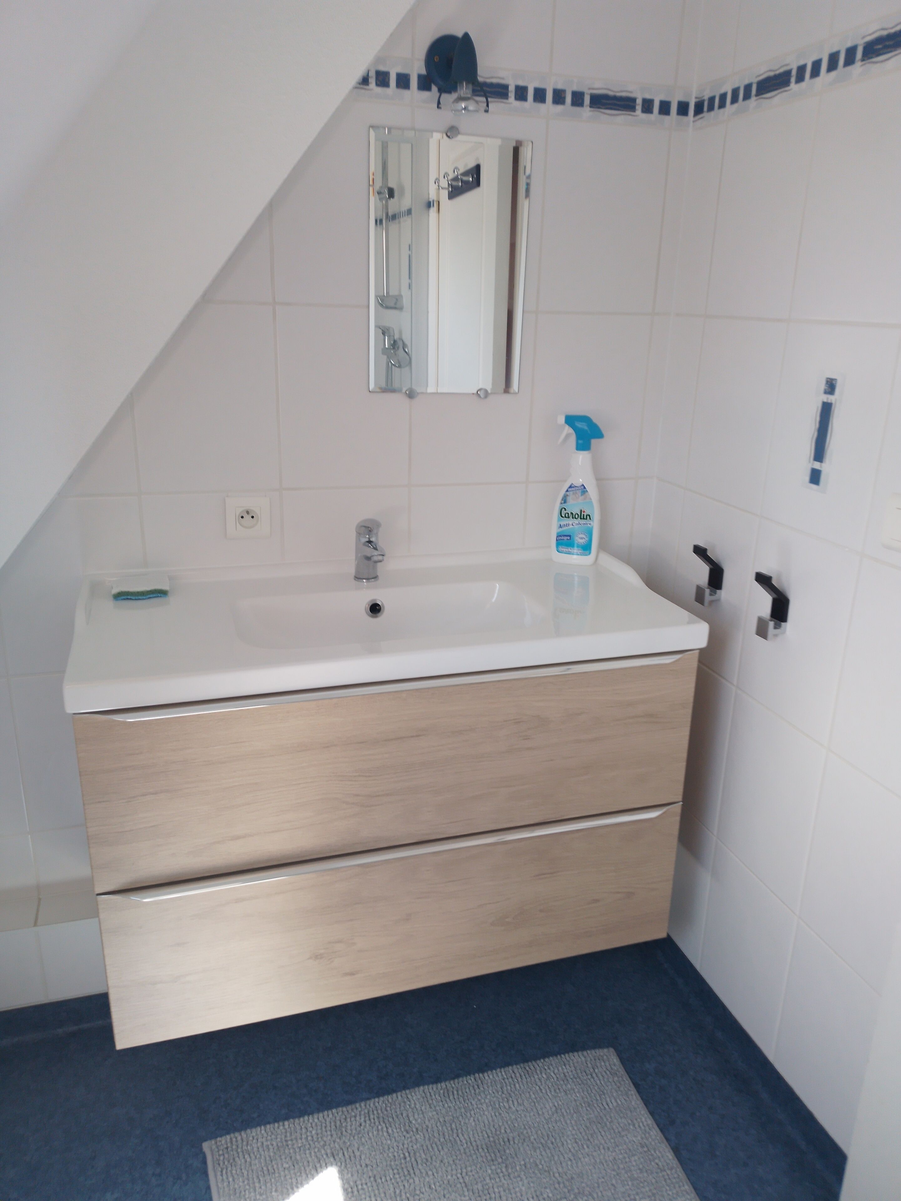 A bathroom with a white sink, wooden drawers, a mirror, and a blue shower curtain.
