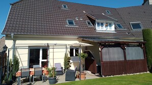 A house with a sloped roof, a covered patio with outdoor furniture, and a fenced yard.