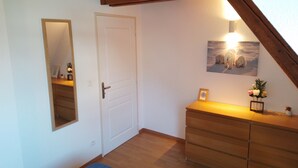 A room with a wooden ceiling, a white door, a dresser, a mirror, and a framed picture on the wall.