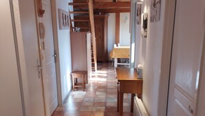 A narrow hallway with tiled flooring, wooden beams on the ceiling, and a staircase leading to an upper level.