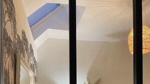 Une pièce chaleureuse avec une lucarne, des meubles à motifs floraux et un vase rempli de fleurs.