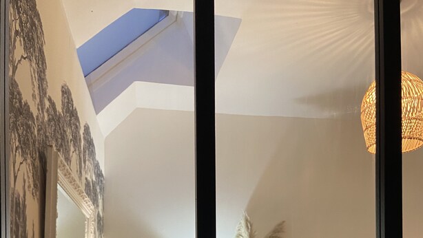 Une pièce chaleureuse avec une lucarne, des meubles à motifs floraux et un vase rempli de fleurs.