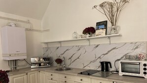 Une cuisine avec des meubles blancs, un pare-feu en marbre, un four encastré, une machine à café et un grille-pain.