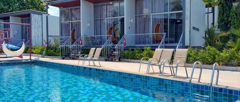 A swimming pool with lounge chairs and a covered seating area.
