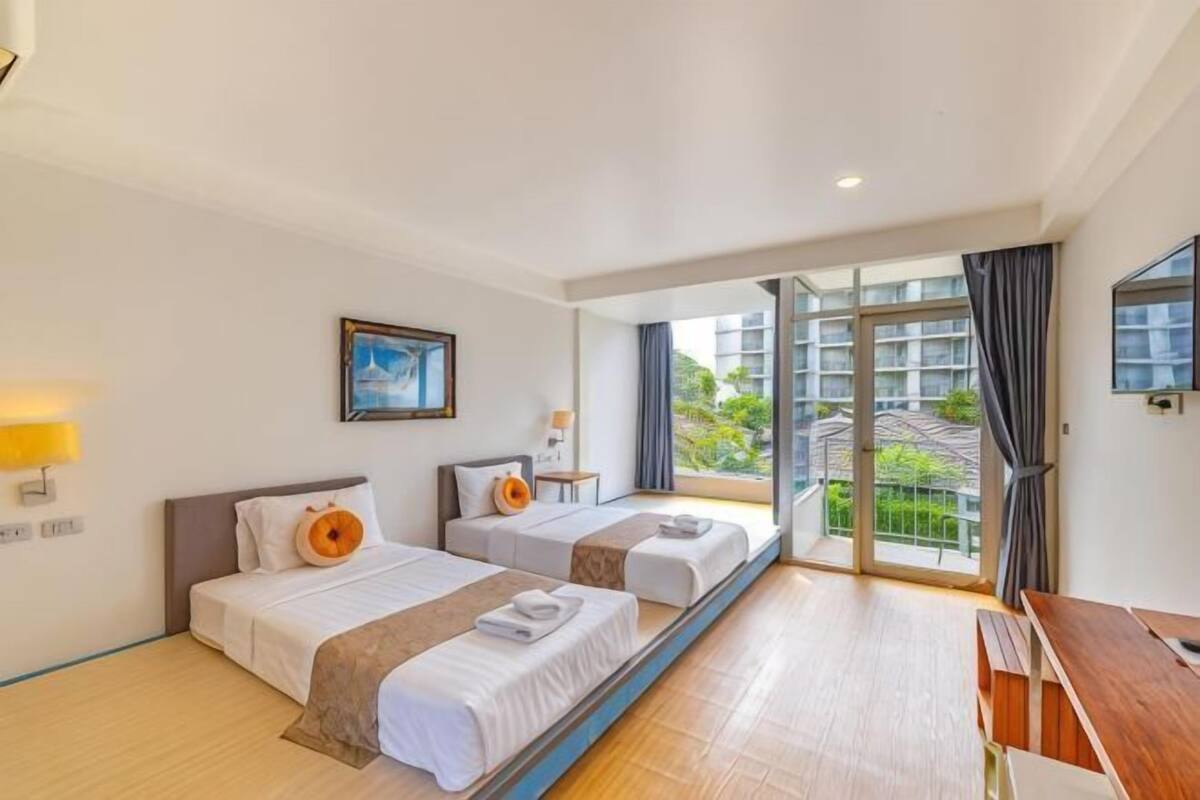 Une chambre d’hôtel avec deux lits, un bureau, une fenêtre donnant sur un paysage agréable et une porte menant à l’extérieur.