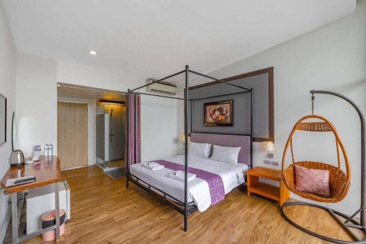 Une chambre d’hôtel moderne avec un lit à baldaquin, un bureau en bois, un fauteuil suspendu et une petite table de chevet.