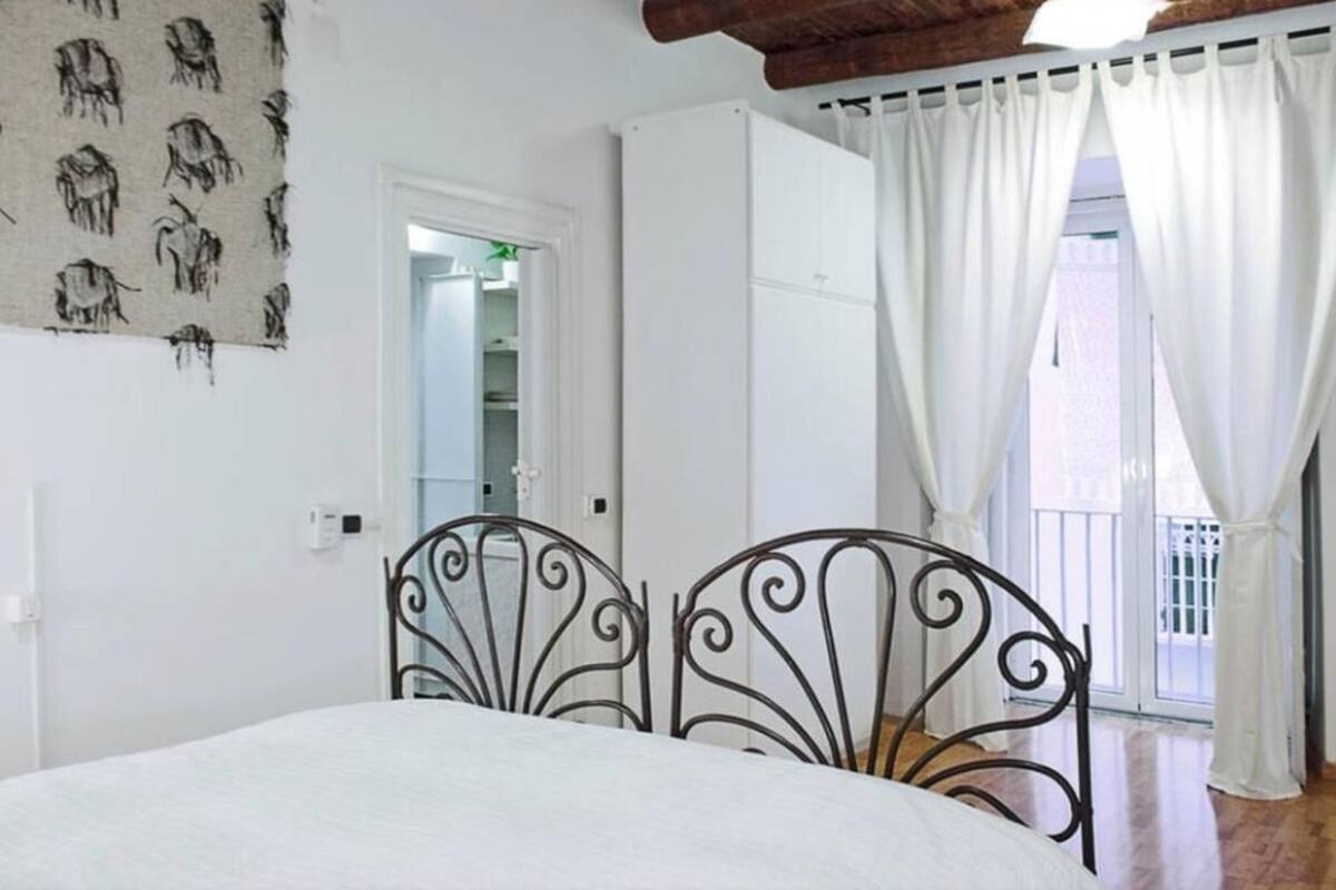 A bedroom with a bed, a wardrobe, a bathroom door, and a balcony with curtains.
