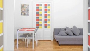 A small, bright room with a white table and chairs, a gray sofa, and a door with colorful panels. - Appartamento Casa toledo (Naples)