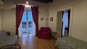 A room with a grey sofa, a red armchair, a patterned bed, and a door leading to a balcony. - Appartamento Casa toledo (Naples)