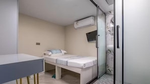 Une petite chambre moderne avec un lit simple, un bureau et un espace douche.