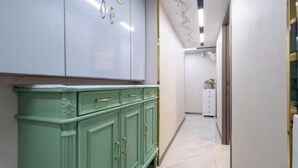 Un couloir avec un meuble vert, un meuble blanc et un sol en marbre.