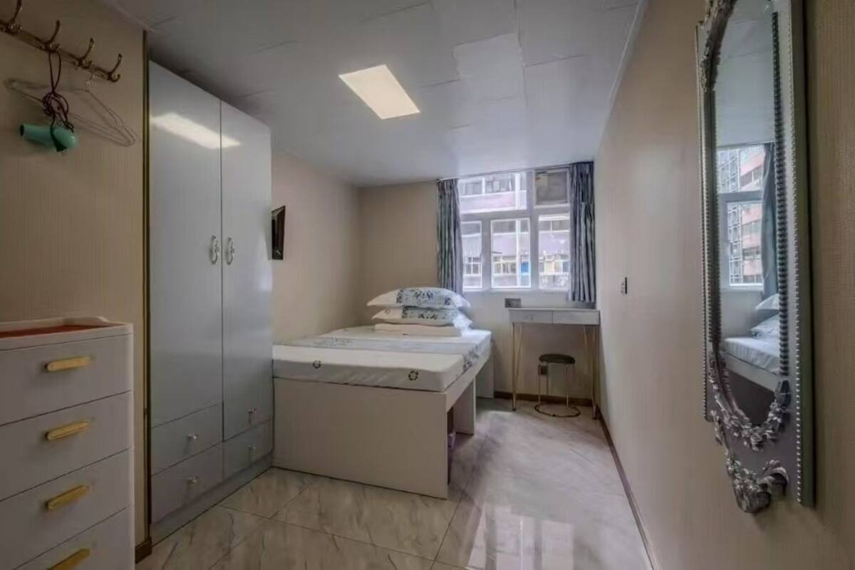 A bedroom with a bed, a wardrobe, a desk, and a large mirror.