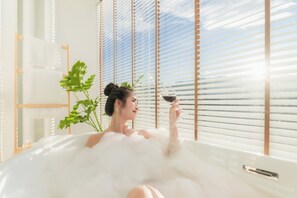 A person in a bathtub with a plant and a window with blinds. - Mai Hotel (Chiang Mai)