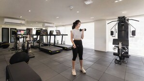 Un gimnasio con cintas de correr, máquinas de pesas y una persona ejercitándose con mancuernas.