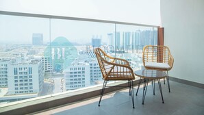 A balcony with two wicker chairs and a table, overlooking a cityscape with modern buildings. - Bloomfields Hidden Gem Studio In Arjan (Dubai)