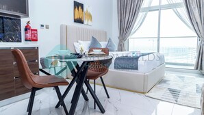 A modern living room with a glass dining table, brown leather chairs, a white sofa, and a large window with curtains. - Bloomfields Hidden Gem Studio In Arjan (Dubai)