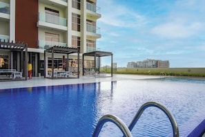A swimming pool with a pergola and lounge chairs, surrounded by a modern building with balconies.