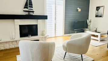 A modern living room with a fireplace, two white armchairs, a flat-screen TV, and a dark grey accent wall.