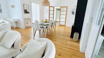 A modern living room with a sofa, a dining table with chairs, and a kitchen area in the background.