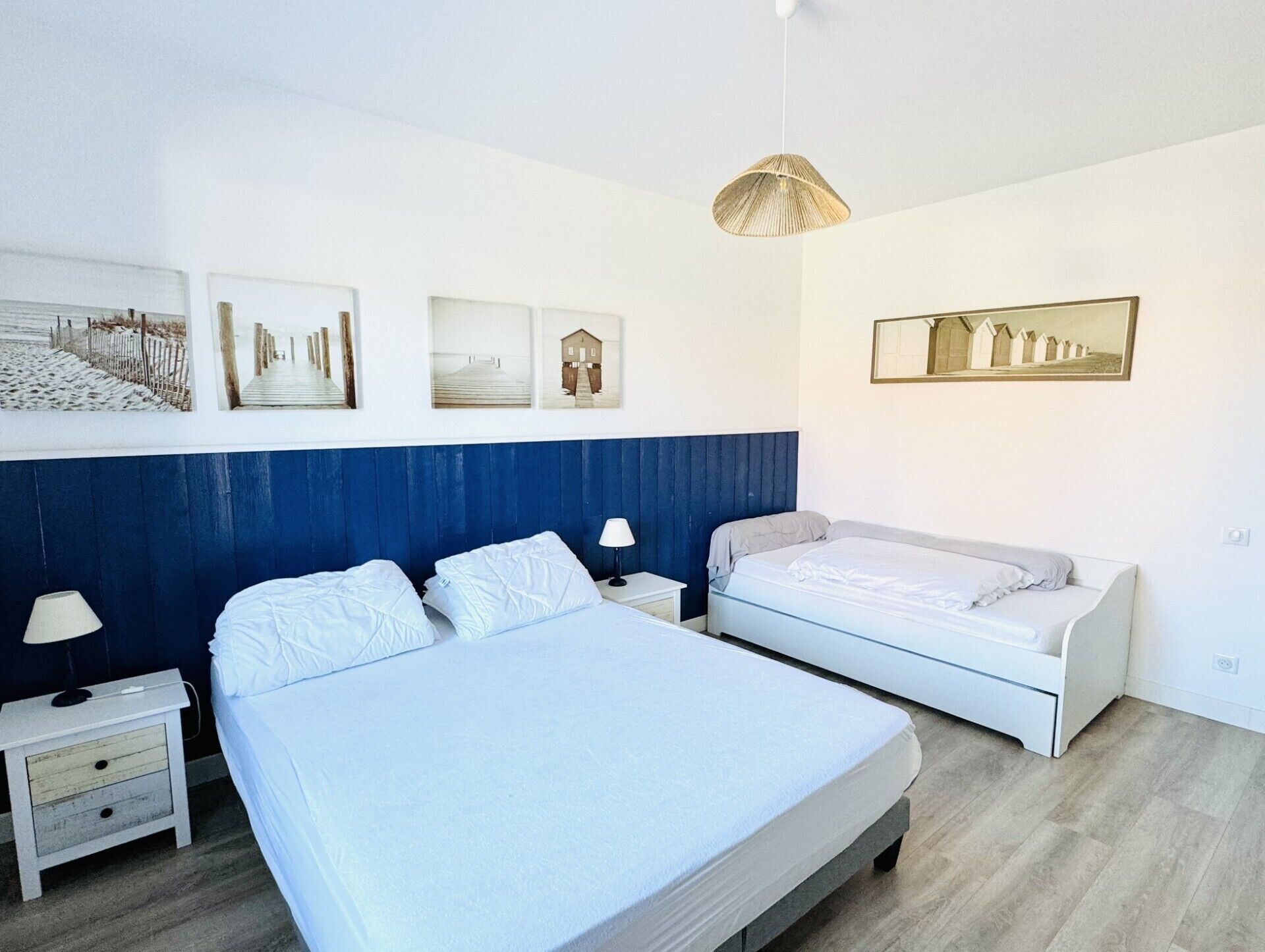 A bedroom with two beds, white bedding, a blue accent wall, and three framed pictures on the wall.