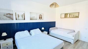 A bedroom with two beds, white bedding, a blue accent wall, and three framed pictures on the wall.