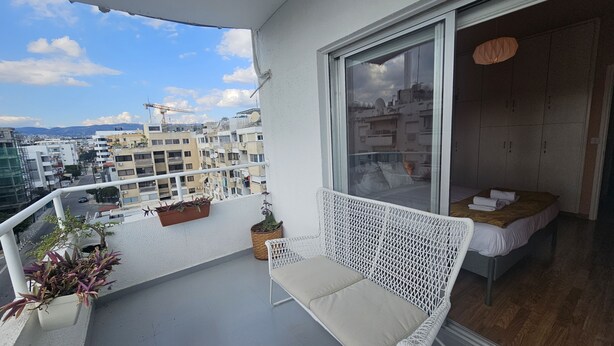 A balcony with a white wicker chair, a small table, and potted plants. - 07 LIM - Stay Velvet Apartment (Limassol)