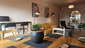 A modern living room with a wooden dining table, a sofa, and a coffee table with a potted plant. There are two black chairs, a laptop on the table, and artwork on the walls. - 07 LIM - Stay Velvet Apartment (Limassol)