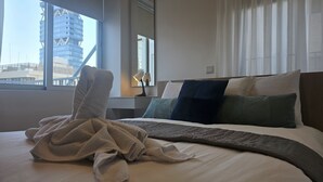 A hotel room with a large bed, a nightstand, a lamp, and a view of a building through the window.