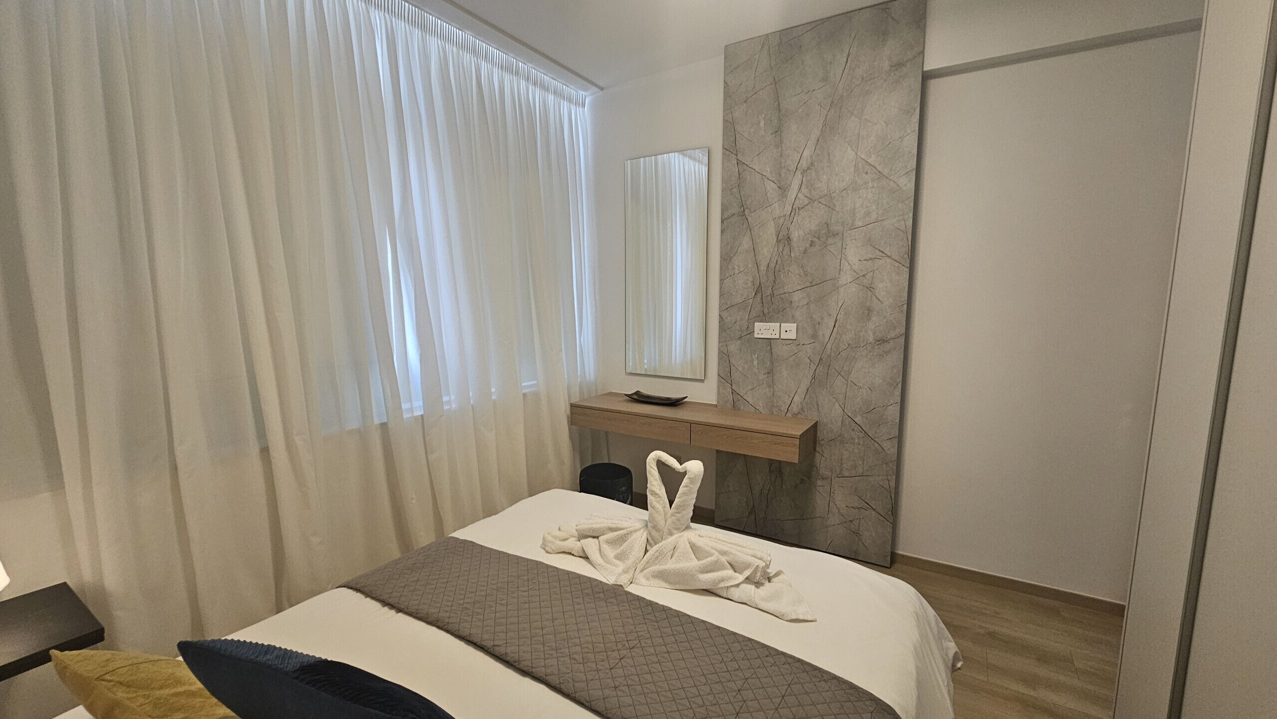 Quarto de hotel com cama, mesa de cabeceira, espelho, parede de mármore e guarda-roupa.