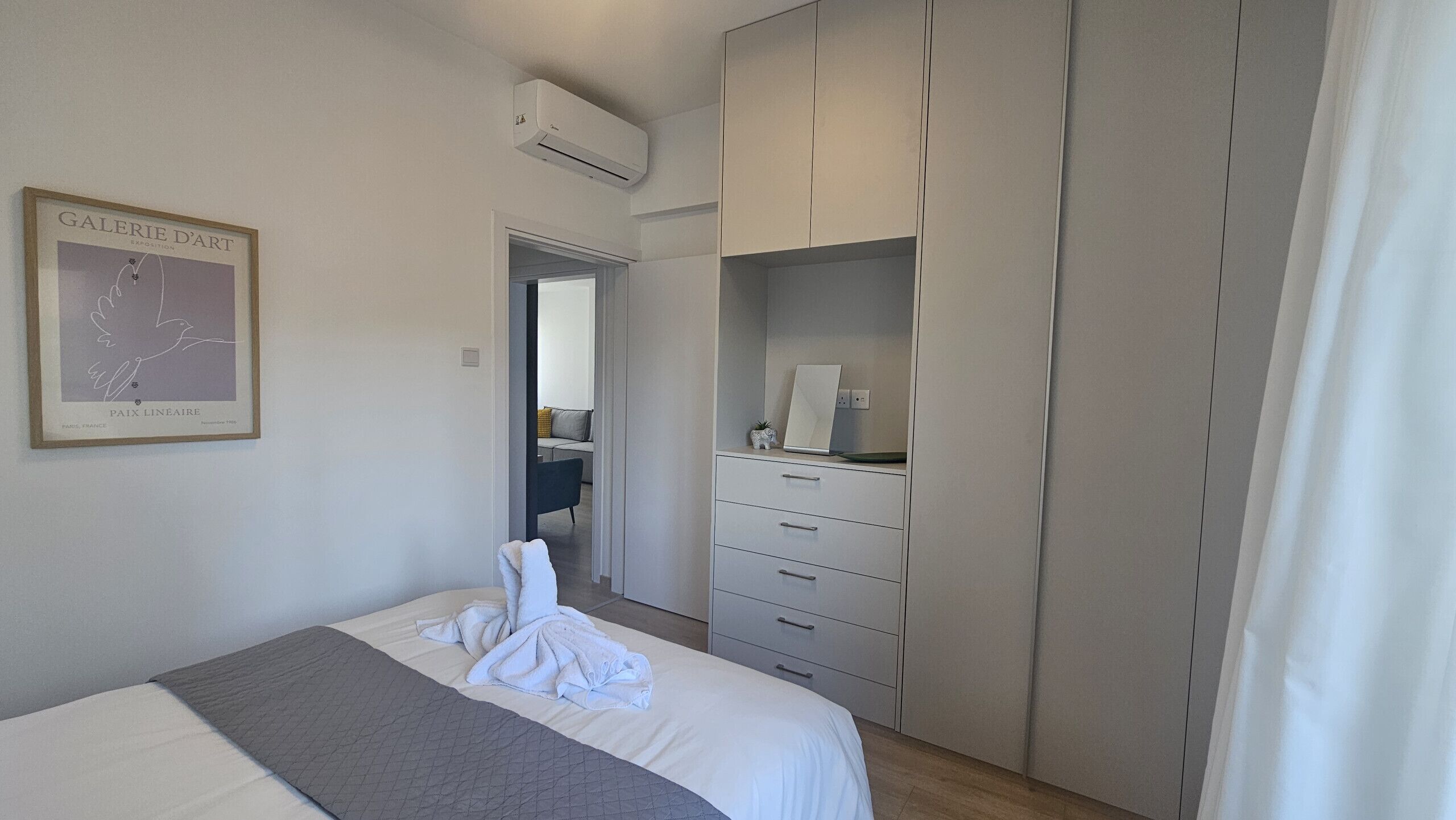 Une chambre à coucher comprenant un lit, une armoire, un miroir et une œuvre d’art encadrée accrochée au mur.
