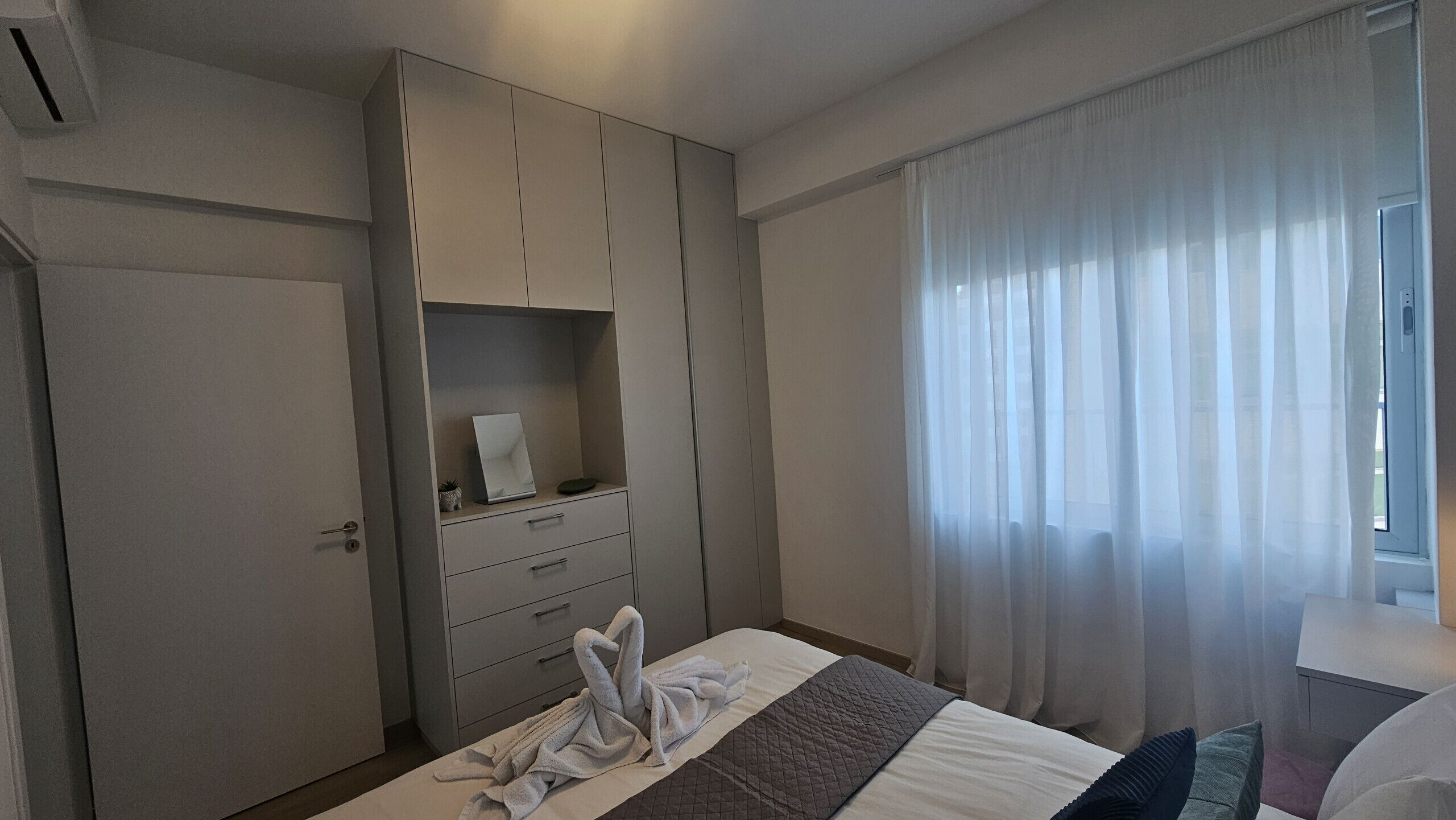 A bedroom with a bed, a wardrobe, a bedside table, and a window with curtains.