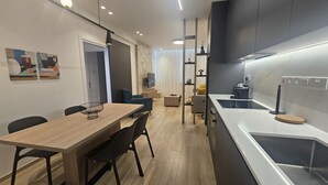 A modern kitchen with a central island, a dining area with a wooden table and chairs, and a living space with a sofa and a TV.