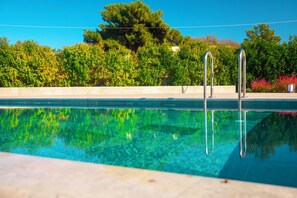 Una piscina con agua cristalina, rodeada por una terraza de concreto y abundante vegetación.