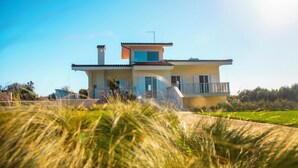 A modern two-story house with a balcony, surrounded by grass and trees. - The FAROS Estate Angelochori - spacious villa with pool to make you feel at home (Angelochori)