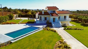 Una casa de dos pisos con piscina, césped cuidado y vista al mar.