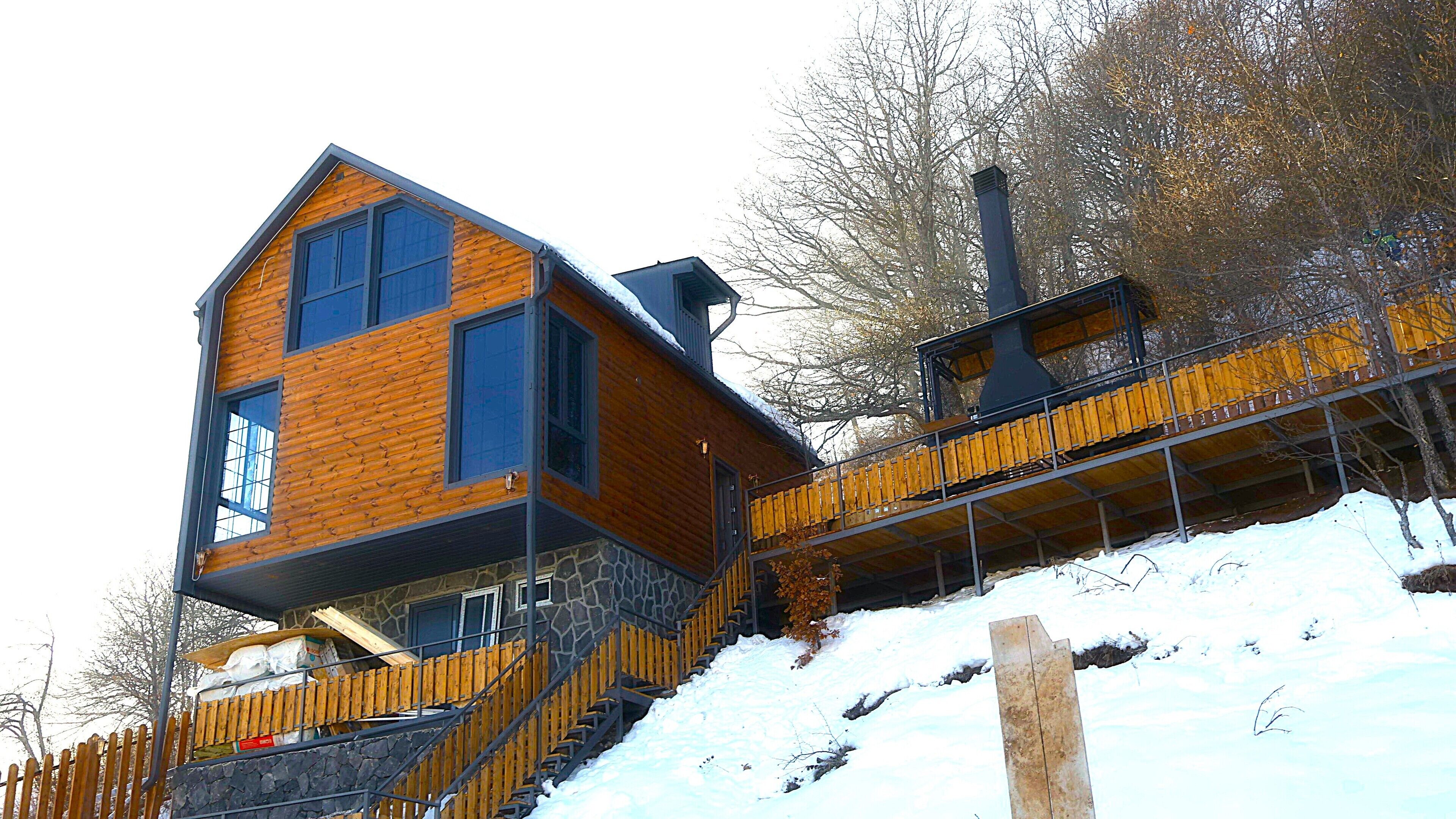 A two-story log cabin with a stone foundation, a chimney, and a wooden deck with a metal railing.