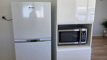 Eine kompakte Küche mit einem weißen Kühlschrank, einer eingebauten Mikrowelle und einem kleinen Schrank.