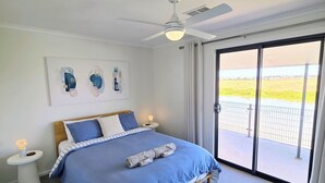 A hotel room with a large bed, a ceiling fan, a nightstand with a lamp, and a view of a field through the sliding glass door. - RiverBed Rise (Tailem Bend)