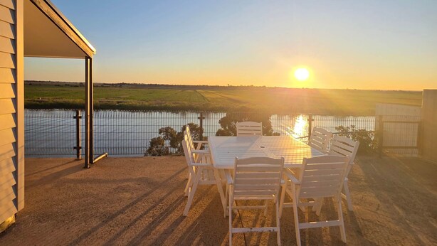 A patio with a table and chairs overlooking a body of water during sunset. - RiverBed Rise (Tailem Bend)
