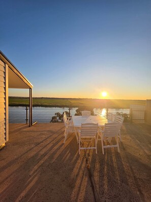 Een terras met een tafel en stoelen met uitzicht op een waterpartij tijdens de zonsondergang.
