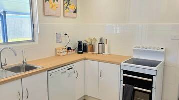 A modern kitchen with white cabinetry, a dishwasher, an oven, and a window with a view of a fence.