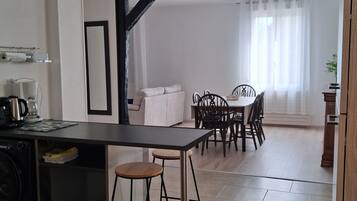 A modern kitchen with a dining area, featuring a central island, bar stools, and a dining table with chairs.