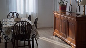 Uma área de jantar com uma mesa posta para quatro pessoas, rodeada por cadeiras. Um armário de madeira com um espelho e um castiçal está encostado na parede.