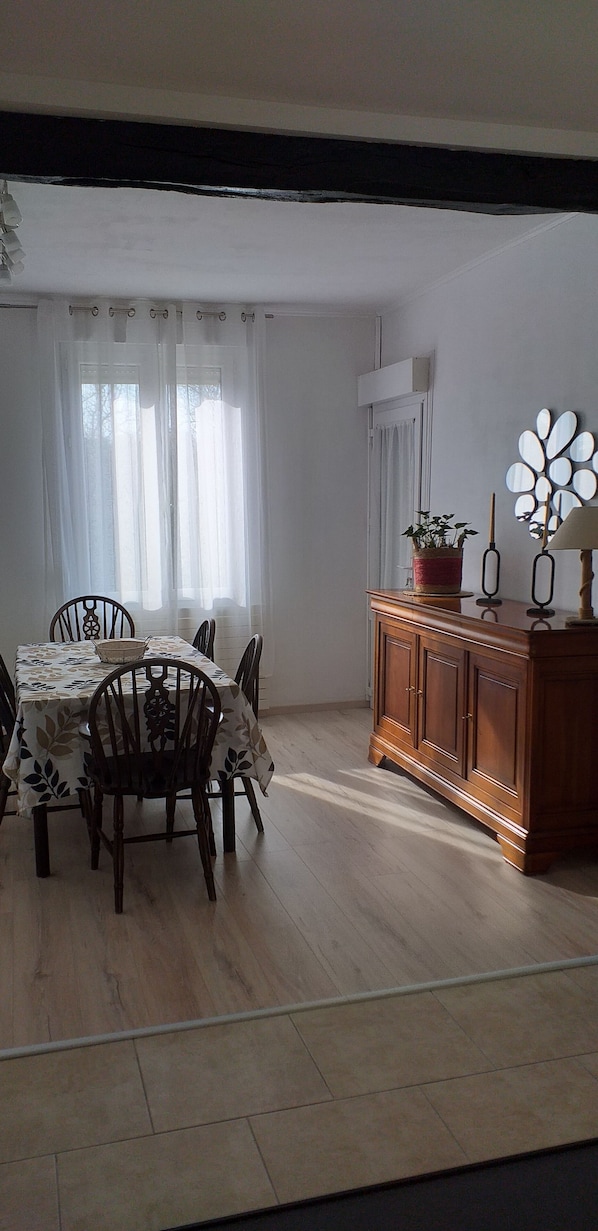A dining area with a table set for four, surrounded by chairs. A wooden cabinet with a mirror and a candle holder is against the wall.