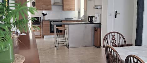 A modern kitchen with wooden cabinets, a central island, and a dining area with wooden chairs.
