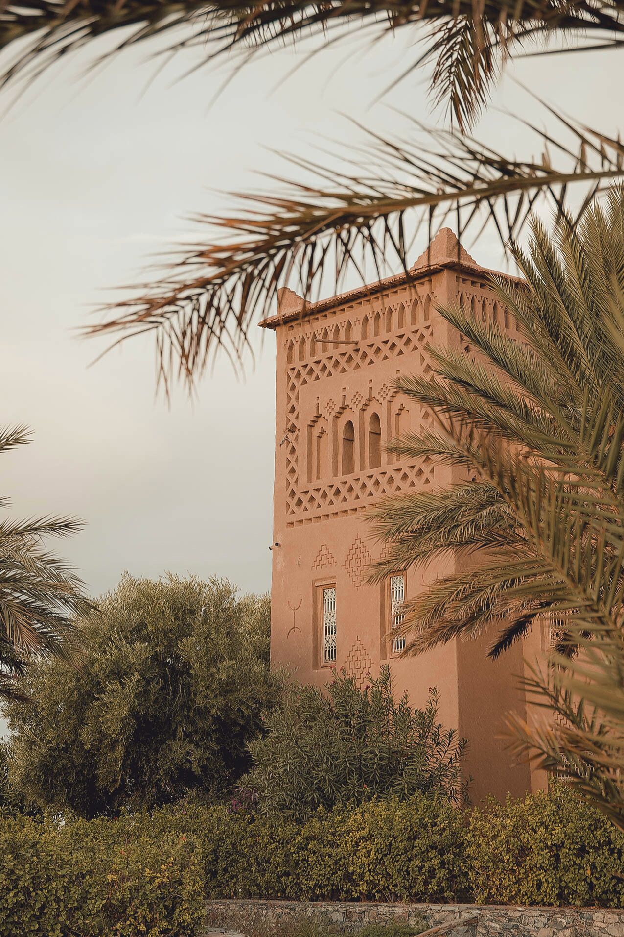 A traditional building with intricate lattice work and arched windows, surrounded by lush greenery.